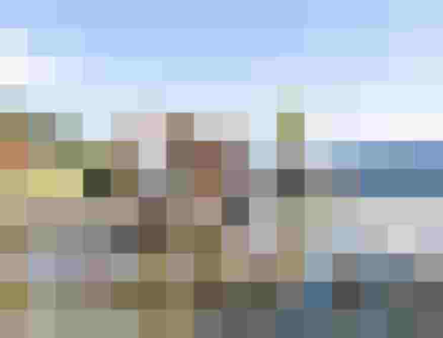 Zwei Kinder balancieren barfuß über Holzpfähle in einem flachen Wasserbereich vor alpiner Landschaft